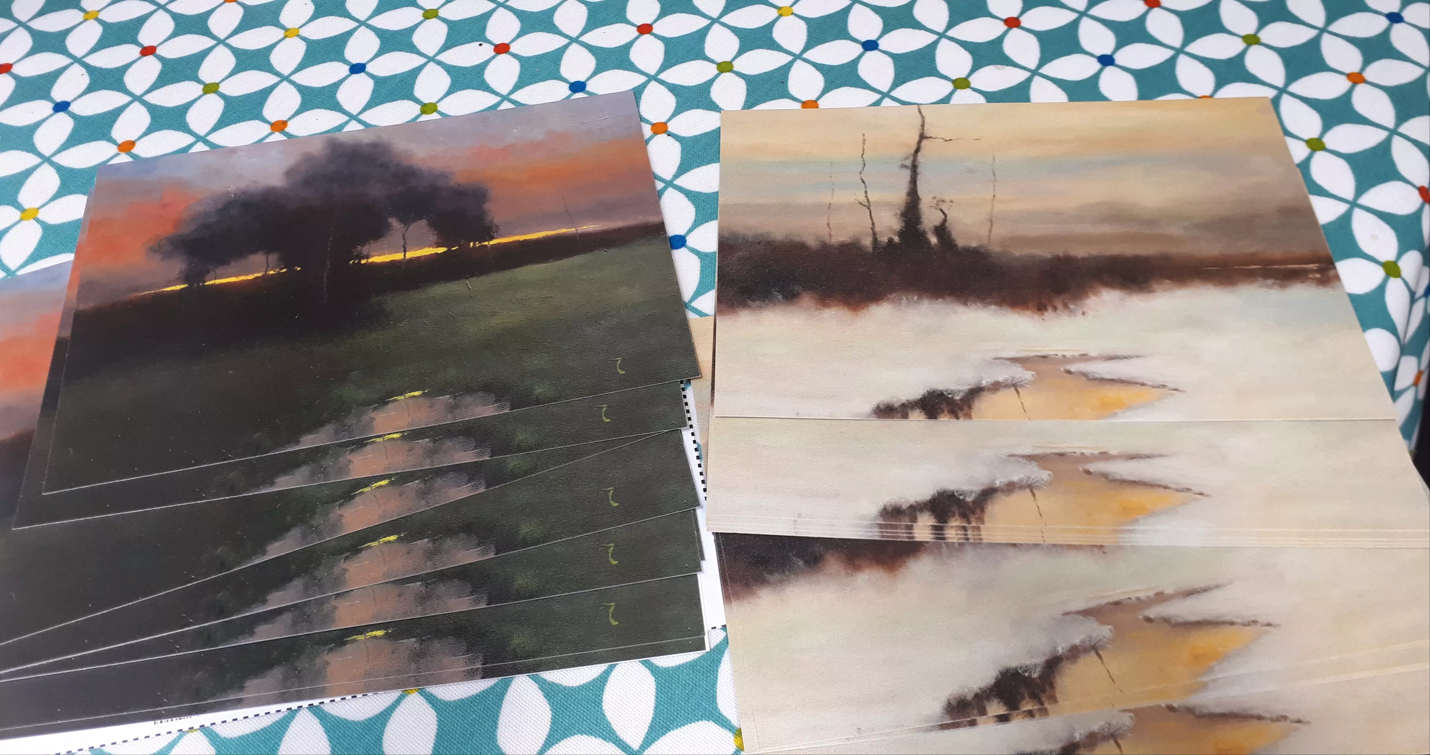 In this last picture we an 
array of postcards spread out in a fan formation. There are 5 postcards in total, all of which are based on gouache paintings. 
At the front of the formation and the only one visible in it's entirety is a post card based on the painting, 'Tall Trees at 
Farran Wood'.